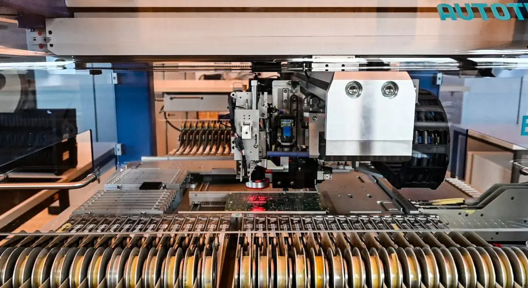 Bestückautomat beim Setzen von Bauteilen auf eine Leiterplatte, davor die Bauteilrollen